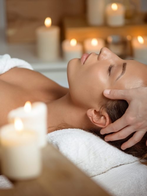 Young beautiful brunette girl having face massage relaxing in spa salon. Eyes closed. Copy space.